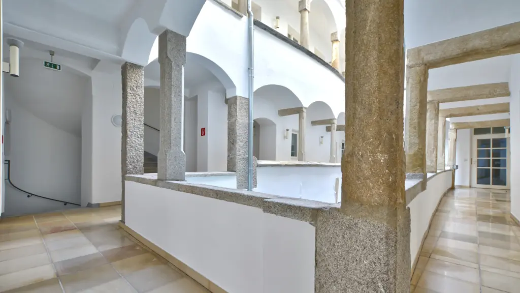 Heller Arkadengang mit Naturstein-Säulen in einem historischen Gebäude.